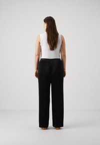 White sleeveless top paired with high-waisted black pleated trousers. Trousers have a smooth texture, resembling a flowing fabric.