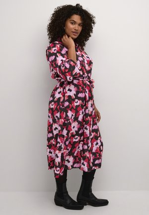 Robe longue à motifs floraux, en noir, rose et blanc, ceinturée à la taille, avec un col et des manches trois-quarts.