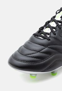 Juodas futbolo batelis su odiniu viršumi, tekstūruota siuvinėjimu, sidabro akcentais, žaliais kaiščiais ir juodomis raištelėmis, matomas iš šono.