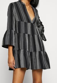 Robe à volants noir et blanc avec un décolleté en V profond, des manches évasées et un motif à rayures verticales comprenant des points et des lignes.