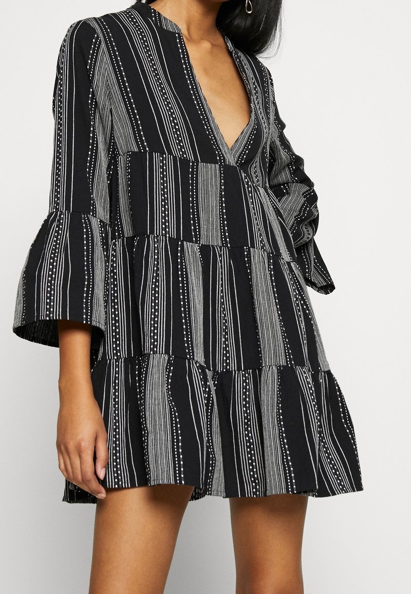 Robe à volants noir et blanc avec un décolleté en V profond, des manches évasées et un motif à rayures verticales comprenant des points et des lignes.