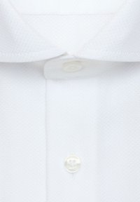 Chemise blanche texturée avec col italien et deux boutons blancs visibles fermés sur la patte de boutonnage avant.