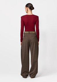 Bordowa bluzka z długim rękawem zestawiona z brązowymi, wysokim stanem spodniami z paskiem w panterk�ę. Tkanina wydaje się gładka i usztywniona.