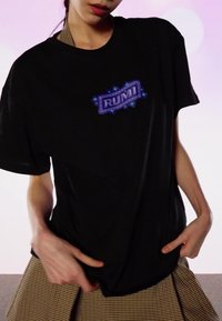 Fekete rövid ujjú póló, lila grafikával és a "RUMI" felirattal. Barna kockás szoknya fölött viselve. Sima szövet textúra.