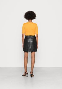 Oranje ribbel gebreid topje met korte mouwen, gecombineerd met een zwarte leren minirok. Zwarte open teen hakken maken de outfit compleet.