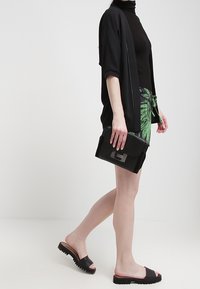 Černý kimono-styl cardigan přes přiléhavé černé tričko, zelené šortky s potiskem, černá kabelka s stříbrným kováním a černé skládací sandály.