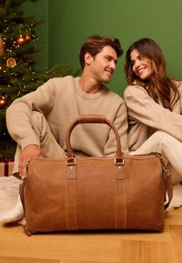 Rudas odinis sportinis krepšys su dviem rankenomis, aukso spalvos detalėmis ir siuvimo akcentais. Lygus paviršius su erdviu dizainu.