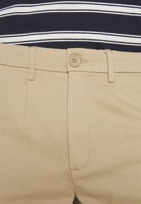 Pantalon kaki en coton à texture lisse, doté de passants pour ceinture, d'une fermeture à un seul bouton et de poches latérales.