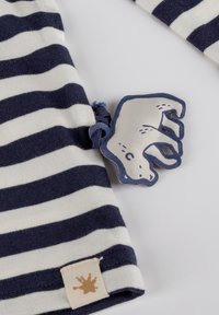 Gestreiftes Langarmoberteil in Marineblau und Creme, mit einem Logo-Tag eines Eisbären, weichem Stoff und einem kleinen dekorativen Spritzetikett am Saum.