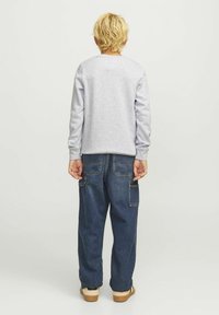 Sudadera gris de manga larga, pantalones cargo azules y zapatos beige. La sudadera tiene un escote redondo y puños de canalé.