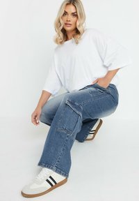 Valkoinen ylipitkä t-paita, vaaleansiniset cargo-housut taskuilla ja valkoiset tennarit mustilla raitoja. Rennoa istuvuutta, sileä kangas, rento tyyli.