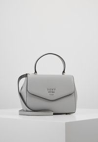 Szara skórzana torebka o usztywnionym kształcie, wyposażona w górny uchwyt oraz odpinany pasek na ramię. Metaliczne logo z przodu.
