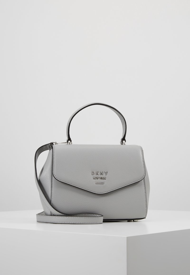 Szara skórzana torebka o usztywnionym kształcie, wyposażona w górny uchwyt oraz odpinany pasek na ramię. Metaliczne logo z przodu.