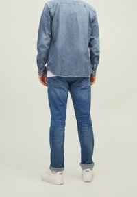 Denimskjorta i ljusblått, långärmad med knapppdetaljer, i kombination med blå jeans och vita sneakers. Bakvy, minimalistisk styling.