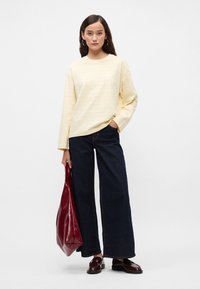 Ανοιχτό κίτρινο μακρυμάνικο πουκάμισο με διακριτές κατακόρυφες ρίγες, συνδυασμένο με σκούρα φαρδιά τζιν και μια βαθιά κόκκινη γυαλιστερή τσάντα. Λείος υφασμάτινος τύπος.