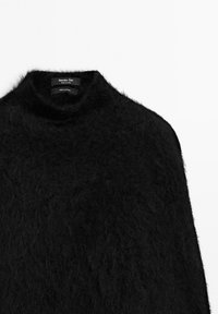 Svart fluffig kashmirtröja med hög krage, som visar en etikett som säger "Massimo Dutti, Tillverkad i Kina."