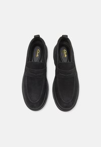 Zapatos negros sin cordones hechos de ante, con un diseño suave, banda elástica y costuras de contraste en los bordes. Interior forrado con material suave.