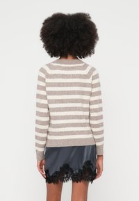 Dryžuotas megztinis smėlio ir baltos spalvų, pagamintas iš minkštos medžiagos, su ilgomis rankovėmis, apvalia iškirpte ir aptempta apačia. Derinamas su sijonu, puoštas nėrinių apvadu.