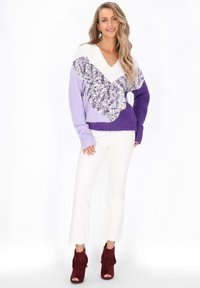 V-Ausschnitt Pullover in lila Tönen mit weißen und silbernen Paillettenakzenten; dicke, gemütliche Stricktextur; kombiniert mit weißen Jeans und burgunderfarbenen Fransenabsätzen.