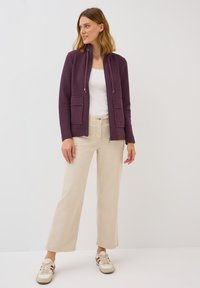 Purple zip-up jacket with a high collar, two front pockets, paired with light beige wide-leg pants and sneakers with stripes.