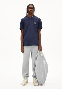 Marineblauw T-shirt met korte mouwen en een klein wit logo, gecombineerd met grijze joggingbroeken en een grijze sweatshirt die vastgehouden wordt. Structuurstof, casual pasvorm.