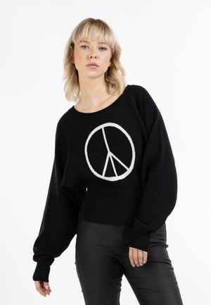 Sort cropped sweater med lange ærmer, der har et hvidt fredstegn design i midten. Glat tekstur og ribbede kantdetaljer.