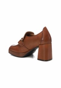 Zapato de cuero marrón con tacón, punta redonda y un destacado detalle de correa. Presenta un tacón ancho y una textura suave.