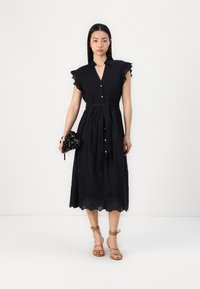 Melna midi kleita ar īsām, viļņotām piedurknēm, priekšējiem pogām un jostu vidusdaļā. Jostas malā ir ziedu izšuvums un gluda tekstūra.