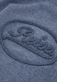Il tessuto blu a maglia presenta un logo ricamato in rilievo di una tonalità abbinata. La trama sembra morbida con sottili variazioni di colore.