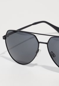 Mustad metallist aviator-prillid tumedate läätsedega ja reguleeritavate ninaümbristega valgel pinnal.