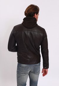 Hnědá kožená bunda s černou kapucí. Má přiléhavý střih, hladkou texturu a kontrastní švy. Pohled ze zad ukazuje vrstvený design.