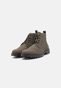 Botines de ante verde oscuro con puntera redonda, cordones negros y suelas de goma texturizadas que cuentan con tacos prominentes para un mejor agarre.
