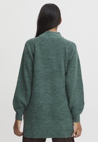 Langärmeliger grüner Pullover mit strukturiertem Strick, gerippten Bündchen und lockerer Passform. Er hat einen hohen Kragen und einen Saum, der unter die Hüften fällt.