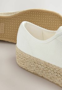 Valge kanvasest tennis, millel on paks kudumisega jute midsole. Omab tekstuuriga kummist välispinda. Lihtne disain minimaalsete õmblustega.