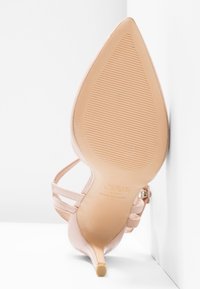 Sandale dénudée à talon avec un bout pointu et de fines brides à la cheville, finition lisse, semelle texturée et talon aiguille. Logo de la marque visible.