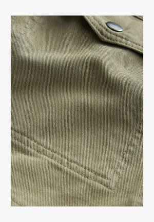 Tissu vert olive avec une texture à côtes fines, doté d'une poche pointue et de détails de couture subtils. Fermoir à pression métallique visible.