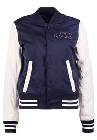 Námořnická bomber bunda s bílými rukávy a pruhovanými manžetami. Disponuje předním logem a dvěma bočními kapsami. Hladká, lehká tkanina.