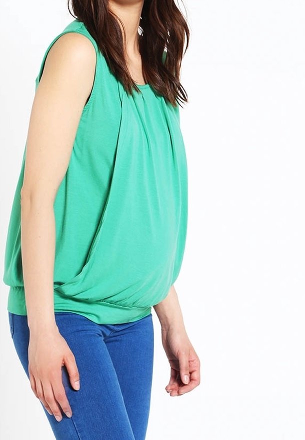 Haut vert sans manches avec plis froncés à l'avant, ourlet arrondi et tissu doux et léger, associé à un jean bleu.