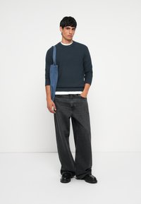 Navy ribbed sweater, white crew neck shirt underneath, loose black jeans, and a blue denim tote bag. Black shoes complete the outfit.