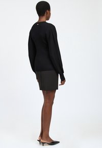 Schwarzer strukturierter Pullover mit langen Ärmeln, kombiniert mit einem dunklen Rock. Slim-Fit, gerippter Schnitt und dezente goldfarbene Hardware-Details auf der Rückseite.