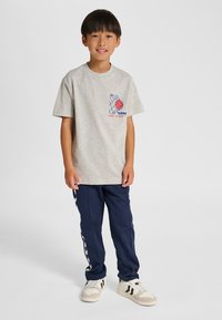 Grijs katoenen T-shirt met blauwe en rode grafische print, gecombineerd met marineblauwe joggingbroek met witte zijstrepen, afgewerkt met witte sneakers.