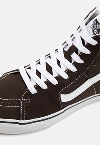 Čierno-biele vysoké tenisky Vans s bielymi šnúrkami, bielym bočným pruhom a logom "Vans Off The Wall" na jazyku.