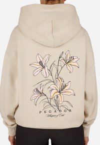 Felpa beige con un grande design floreale che presenta gigli rosa sul retro. Testo "PEGADOR" e "Whispers of Cold" in un carattere decorativo.