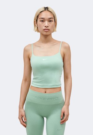 Jeune personne portant des leggings Nike Pro vert pâle et un débardeur court assorti, debout devant un fond clair et uni.