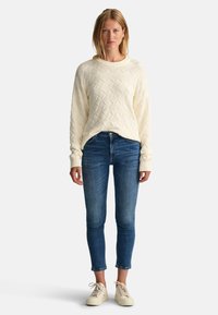 Krämfärgad kabelstickad tröja med rund hals, matchad med åtsittande blå denim jeans och ljusa sneakers.