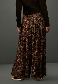 Wide-leg pants in a leopard print pattern featuring browns and blacks. Made of soft fabric with a pleated design and elastic waistband.