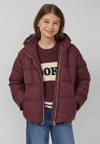 Bordo zimska jakna s kapuljačom, s kockastim dizajnom i prednim zatvaračem. Nosena preko pletenog pulovera s krem i crnim prugama.