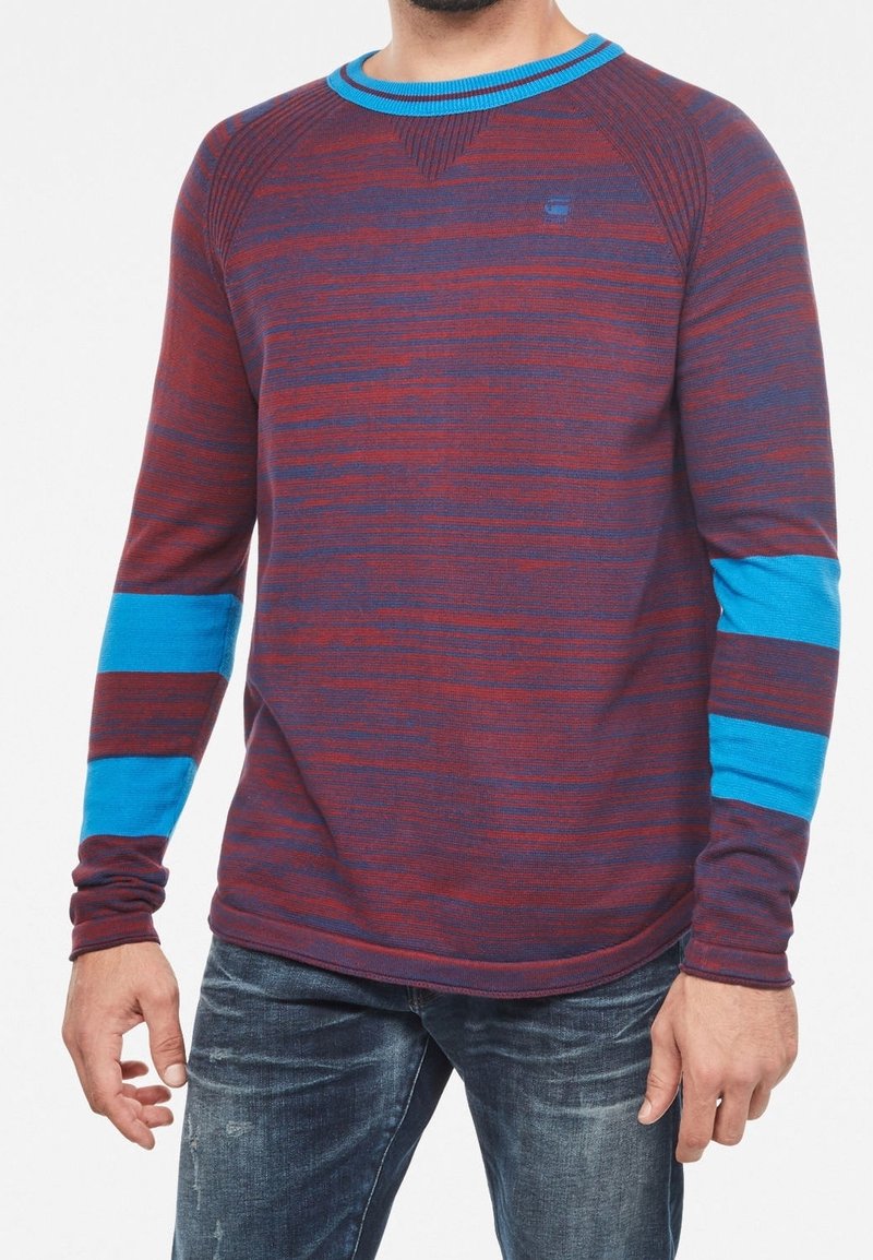Pull à manches longues présentant un motif rayé bordeaux et bleu, une texture côtelée et un col rond avec des accents bleus contrastants sur les manches.