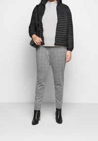 Giacca imbottita nera, maglione lavorato a maglia grigio chiaro, pantaloni grigi a quadri e stivaletti neri con tacco. Materiali lisci e strutturati.