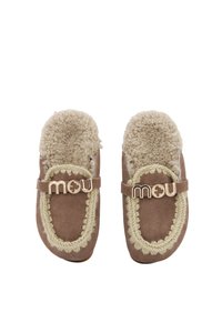 Zapatillas de ante marrón con forro de shearling beige, costuras decorativas y una correa con la marca que presenta un logotipo en tono dorado.